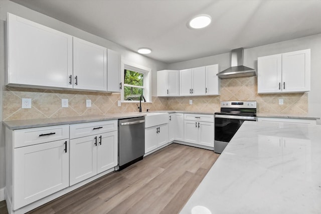kitchen featuring wall chimney range hood, light stone counters, white cabinetry, light wood-style flooring, and stainless steel appliances