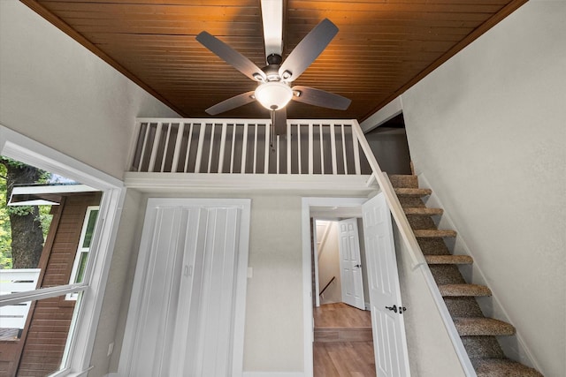 stairway with wood finished floors, a ceiling fan, a towering ceiling, and wood ceiling