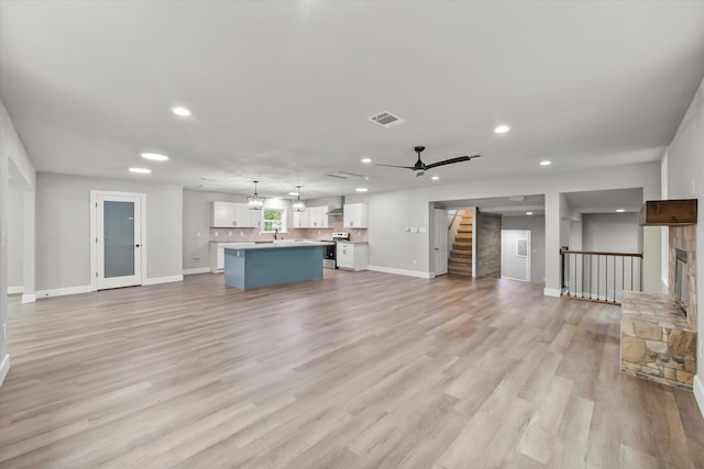 unfurnished living room featuring light wood-type flooring, ceiling fan with notable chandelier, and a fireplace