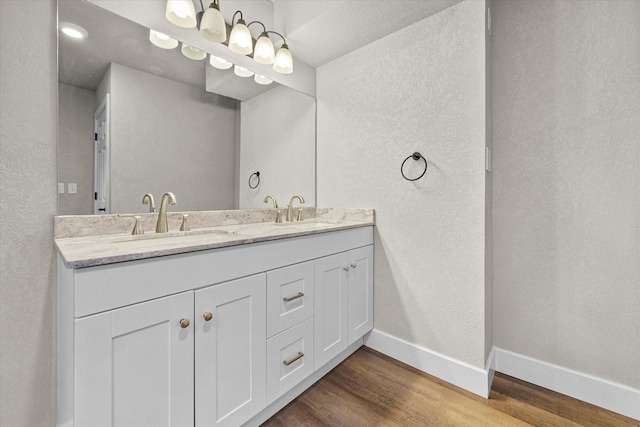 bathroom featuring double vanity, wood finished floors, baseboards, and a sink