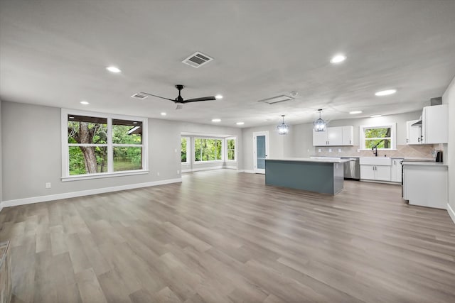 unfurnished living room with ceiling fan, light hardwood / wood-style flooring, sink, and a healthy amount of sunlight