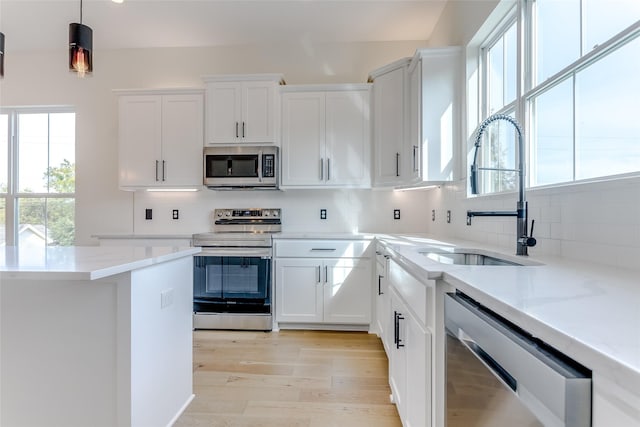 kitchen featuring stainless steel appliances, backsplash, white cabinetry, a sink, and light wood-type flooring