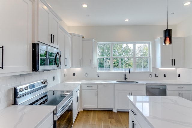 kitchen featuring light wood finished floors, appliances with stainless steel finishes, a sink, and white cabinets