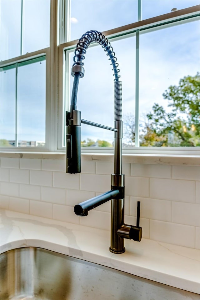 interior details with light stone counters, a sink, white cabinetry, and decorative backsplash