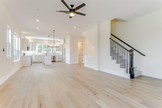 unfurnished living room featuring recessed lighting, stairway, light wood-type flooring, baseboards, and ceiling fan with notable chandelier