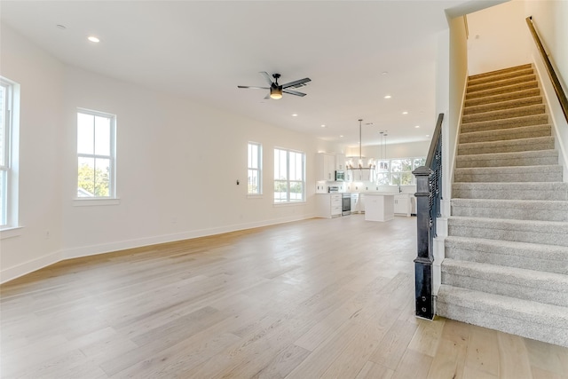 unfurnished living room with recessed lighting, baseboards, light wood-style flooring, stairway, and ceiling fan with notable chandelier