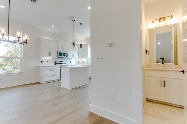 kitchen with appliances with stainless steel finishes, a center island, light countertops, white cabinetry, and backsplash