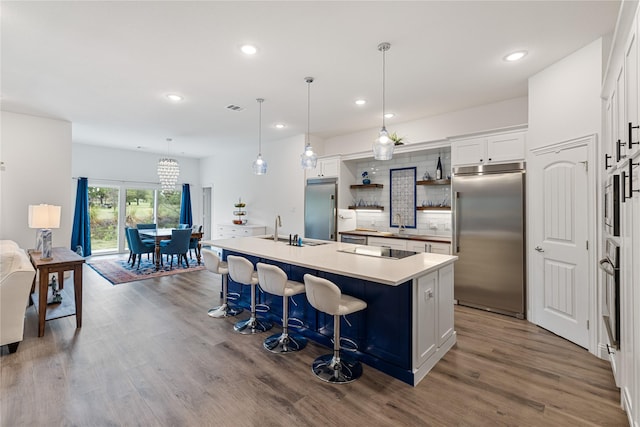 kitchen featuring stainless steel appliances, decorative light fixtures, a center island with sink, and white cabinets