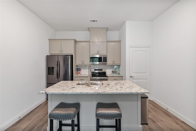 kitchen featuring light hardwood / wood-style floors, light stone countertops, an island with sink, and appliances with stainless steel finishes