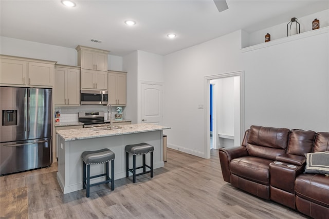 kitchen featuring light hardwood / wood-style flooring, appliances with stainless steel finishes, a kitchen island with sink, light stone counters, and a kitchen bar