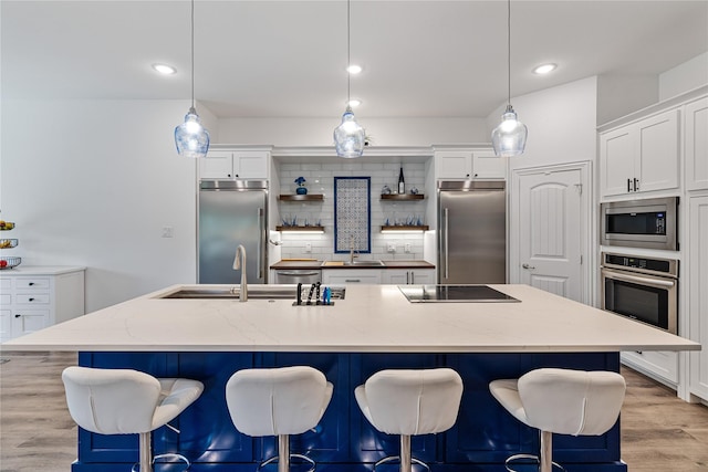 kitchen featuring a center island with sink, white cabinetry, built in appliances, and decorative light fixtures