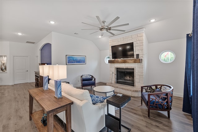 living room with vaulted ceiling, ceiling fan, a stone fireplace, and hardwood / wood-style floors