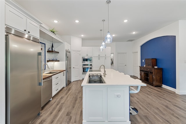 kitchen with a center island with sink, white cabinetry, built in appliances, and decorative light fixtures