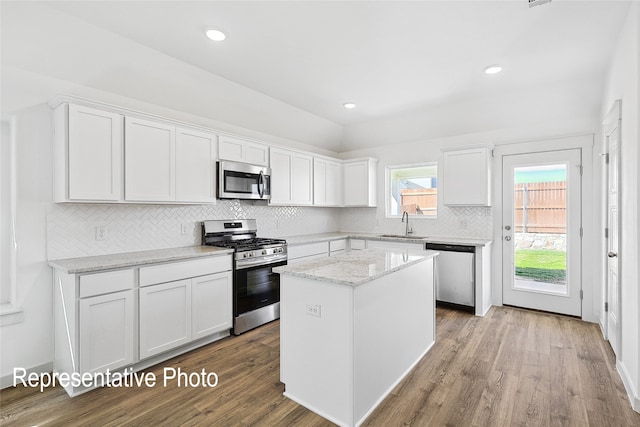 kitchen featuring a center island, white cabinets, light wood-type flooring, light stone countertops, and stainless steel appliances