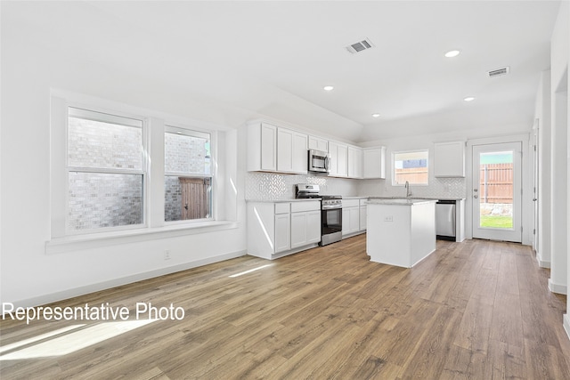 kitchen featuring light hardwood / wood-style flooring, decorative backsplash, appliances with stainless steel finishes, a kitchen island, and white cabinetry