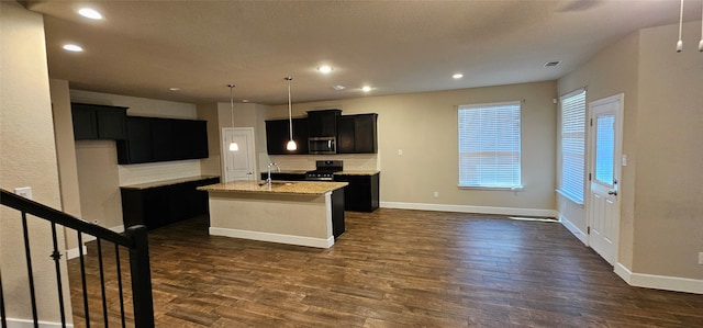 kitchen featuring dark wood-type flooring, light stone counters, range, a center island with sink, and decorative backsplash