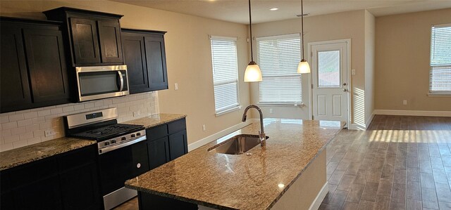 kitchen featuring stainless steel dishwasher, an island with sink, light stone countertops, and sink