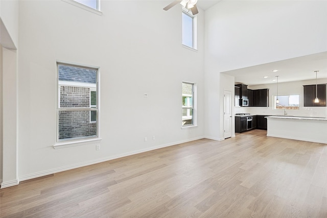3913 Sky Dr, Sherman, TX 75090 - unfurnished living room with ceiling fan, light wood-style floors, a towering ceiling, a sink, and baseboards