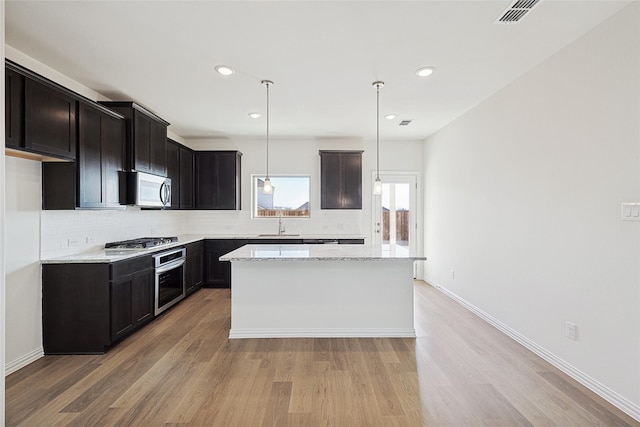 kitchen with hanging light fixtures, appliances with stainless steel finishes, a kitchen island, light stone countertops, and decorative backsplash