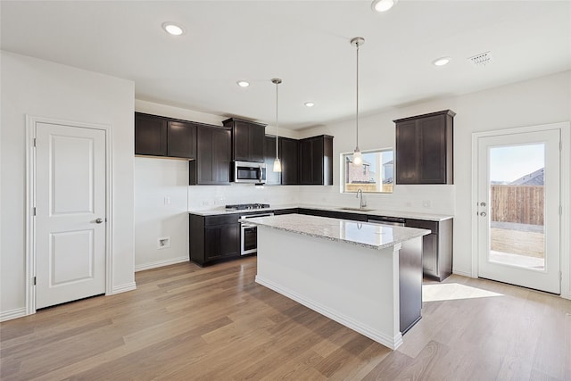 kitchen with sink, hanging light fixtures, a center island, light stone counters, and stainless steel appliances