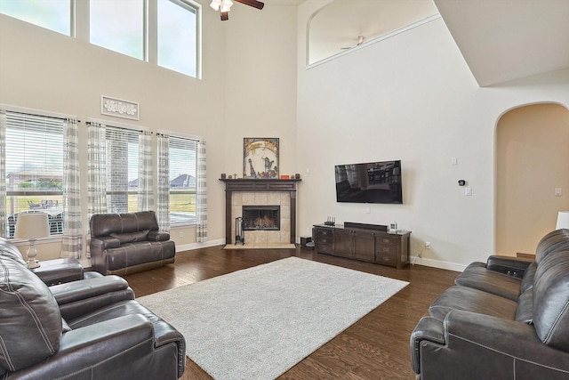 living room with a tiled fireplace, dark hardwood / wood-style flooring, a high ceiling, and ceiling fan