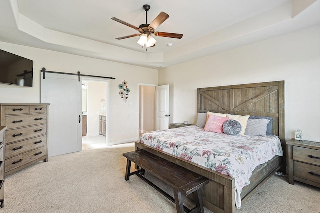 bedroom with a raised ceiling, connected bathroom, ceiling fan, and a barn door