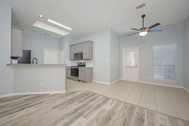 kitchen with gray cabinets, light tile patterned flooring, kitchen peninsula, stainless steel appliances, and ceiling fan