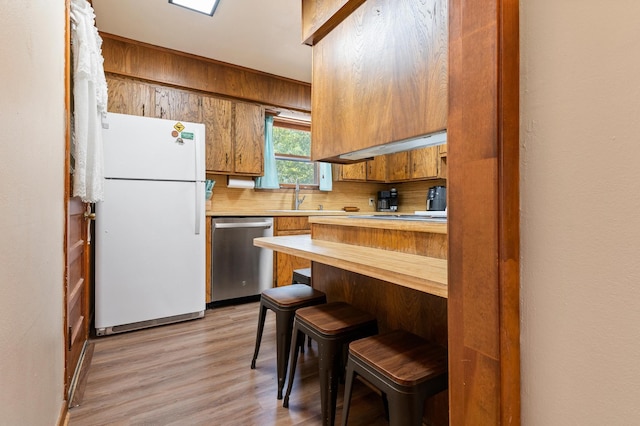 kitchen featuring dishwasher, white refrigerator, light hardwood / wood-style flooring, a kitchen breakfast bar, and backsplash