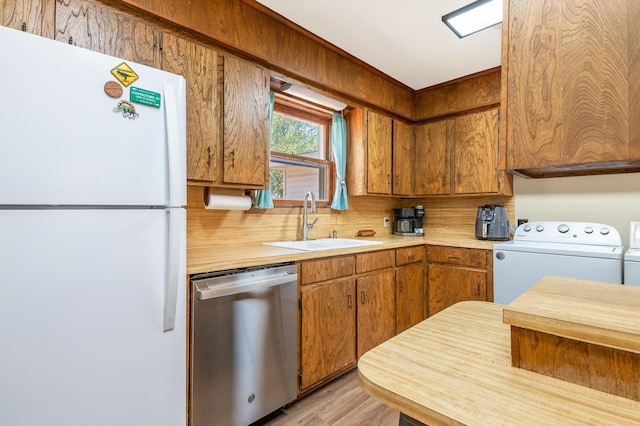 kitchen featuring white refrigerator, dishwasher, light wood-type flooring, washer / dryer, and sink