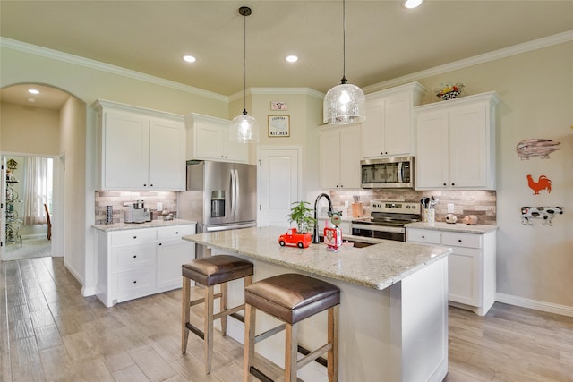 kitchen with white cabinets, an island with sink, stainless steel appliances, and light hardwood / wood-style flooring