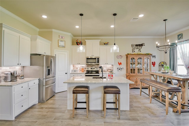 kitchen with light stone counters, white cabinets, a center island with sink, appliances with stainless steel finishes, and an inviting chandelier