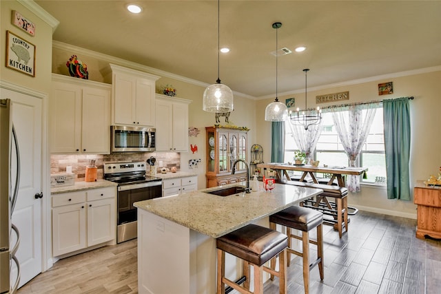 kitchen with white cabinets, appliances with stainless steel finishes, a kitchen island with sink, and sink