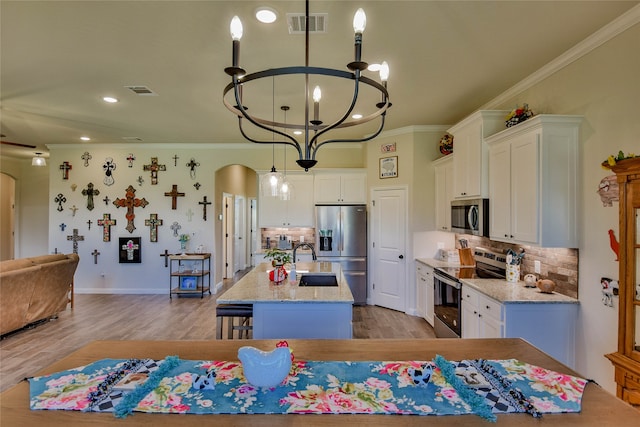 kitchen featuring a kitchen island with sink, white cabinetry, hanging light fixtures, light hardwood / wood-style flooring, and stainless steel appliances