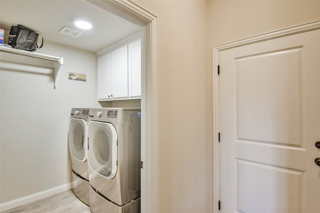 laundry room featuring washing machine and clothes dryer, light wood-type flooring, and cabinets