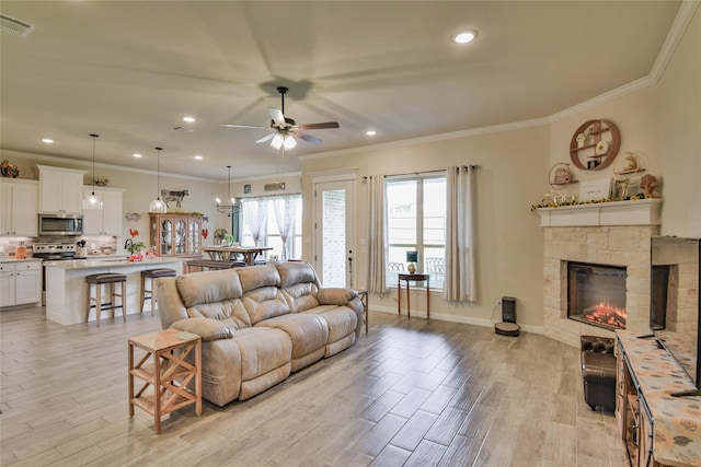 living room with light hardwood / wood-style flooring, ceiling fan, crown molding, and a stone fireplace