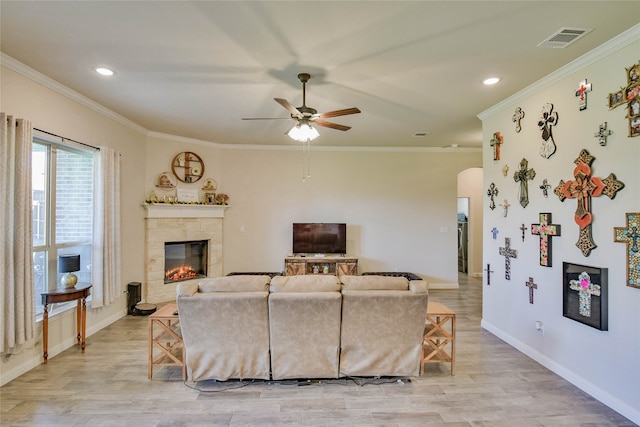 living room featuring light wood-type flooring, ceiling fan, a fireplace, and crown molding