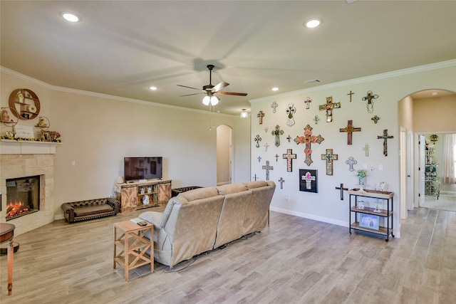 living room with light hardwood / wood-style flooring, ornamental molding, ceiling fan, and a fireplace