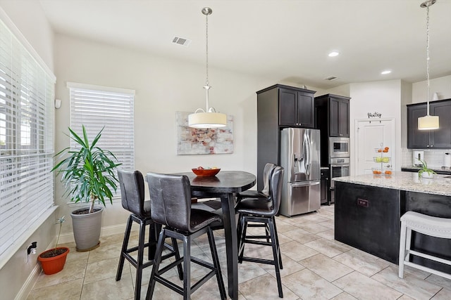 kitchen featuring decorative backsplash, a kitchen breakfast bar, stainless steel appliances, light stone countertops, and decorative light fixtures