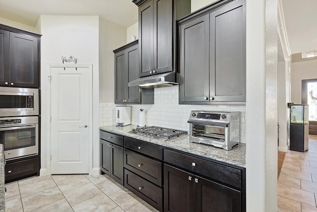 kitchen with backsplash, light stone countertops, dark brown cabinetry, light tile patterned floors, and appliances with stainless steel finishes