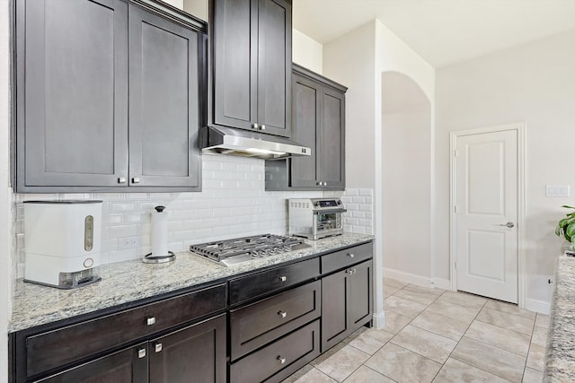 kitchen featuring stainless steel gas stovetop, tasteful backsplash, light stone counters, and light tile patterned floors