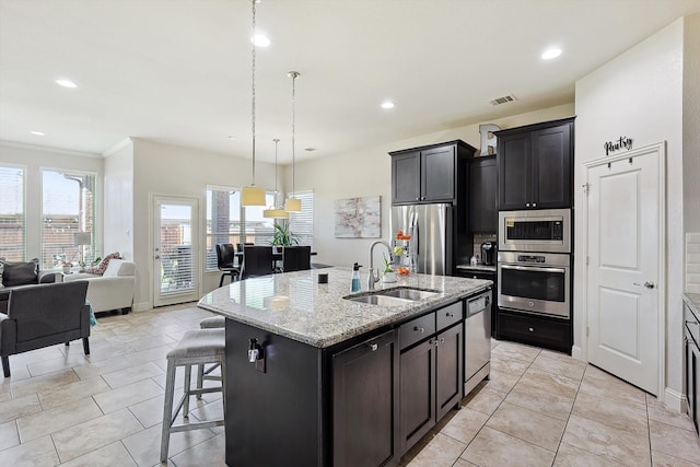 kitchen featuring an island with sink, ornamental molding, sink, appliances with stainless steel finishes, and light stone counters