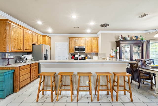 kitchen with a kitchen breakfast bar, stainless steel appliances, light tile patterned floors, and ornamental molding