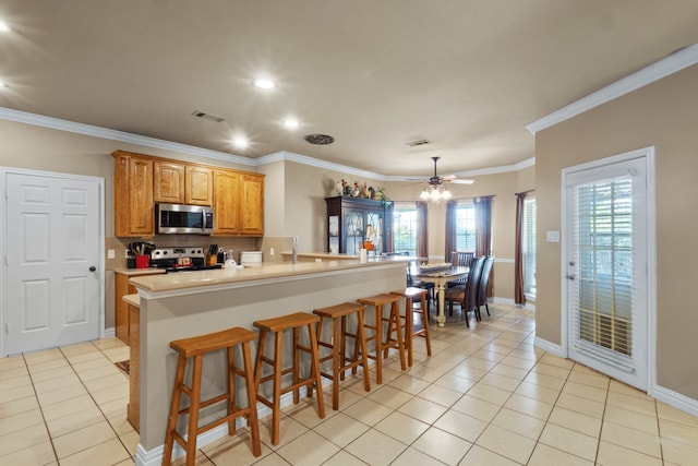 kitchen with appliances with stainless steel finishes, light tile patterned flooring, a breakfast bar area, crown molding, and ceiling fan