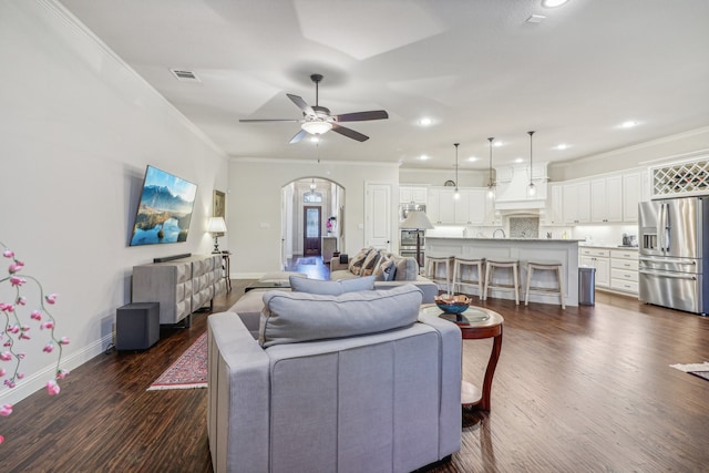 living room featuring ceiling fan with notable chandelier, a stone fireplace, crown molding, and dark wood-type flooring