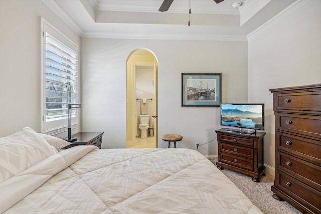 carpeted bedroom with a tray ceiling, ensuite bath, ceiling fan, and crown molding