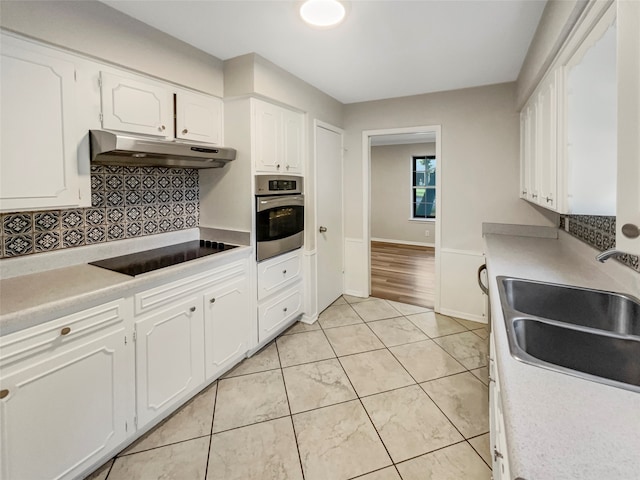 kitchen featuring sink, oven, white cabinetry, black electric cooktop, and decorative backsplash