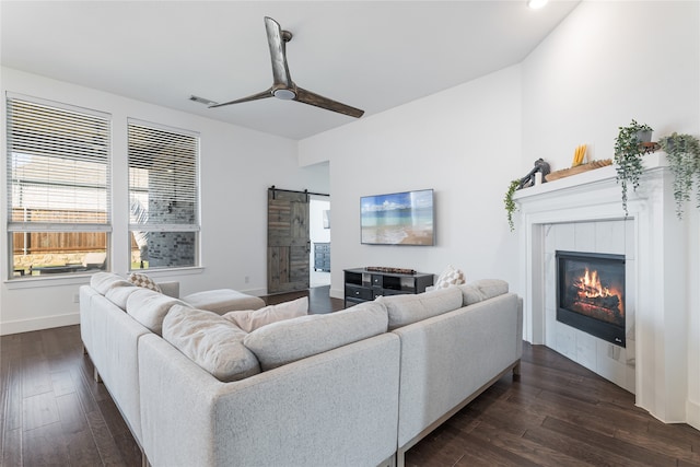 living room with ceiling fan, a barn door, dark hardwood / wood-style flooring, and a tile fireplace