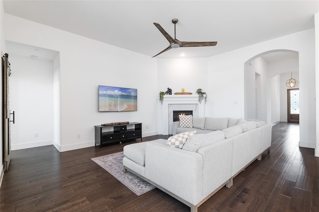 living room with a tiled fireplace, ceiling fan, and dark wood-type flooring