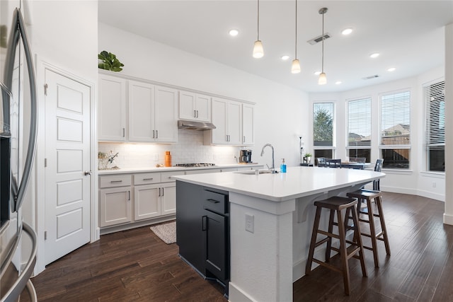 kitchen with a center island with sink, decorative light fixtures, white cabinetry, and dark wood-type flooring