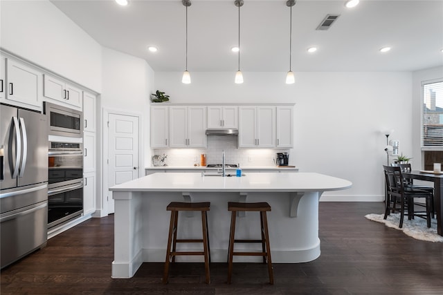 kitchen with a kitchen island with sink, white cabinets, hanging light fixtures, dark hardwood / wood-style floors, and stainless steel appliances